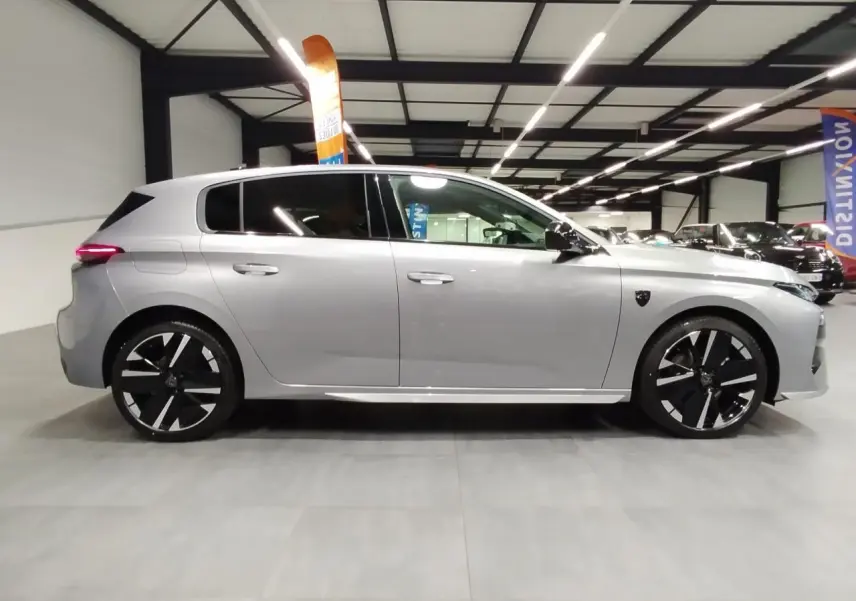 Profil droit d'une Peugeot 308 gris Artense avec jantes alliage noires et toit noir en intérieur d'exposition.