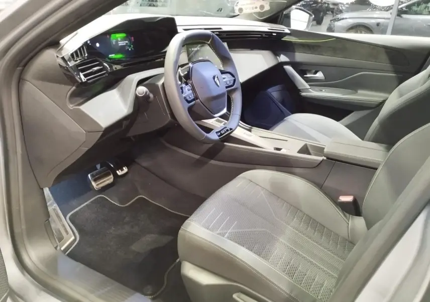Vue intérieure côté conducteur de la Peugeot 308 gris Artense, avec volant compact GT et tableau de bord numérique 3D.