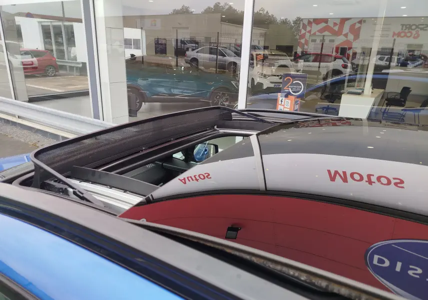 Vue rapprochée du toit ouvrant panoramique du Kia Sportage bleu fusion métallisé, avec reflet du showroom.