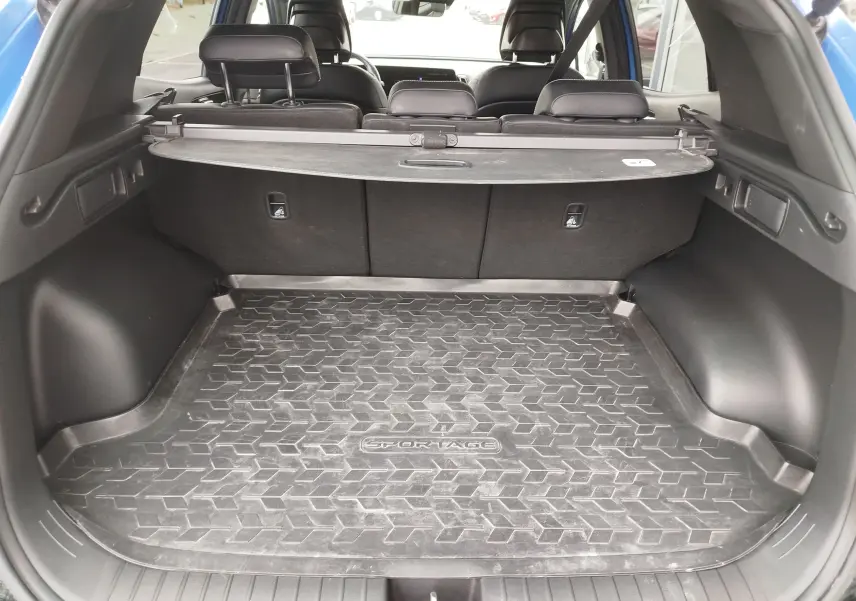 Coffre ouvert du KIA SPORTAGE bleu Fusion, vue arrière montrant la protection de coffre en caoutchouc avec logo Sportage.