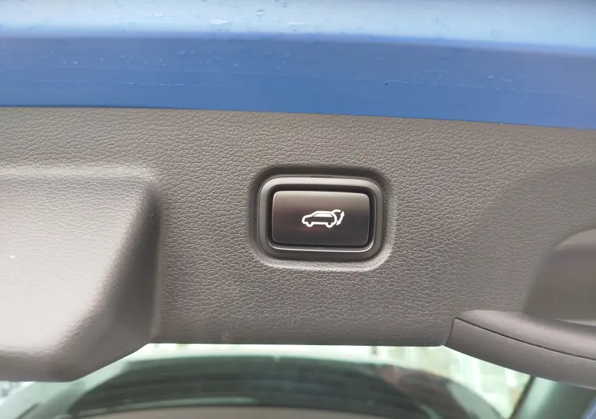 Bouton de fermeture électrique du hayon sur la partie intérieure du coffre d'un KIA Sportage bleu métallisé.