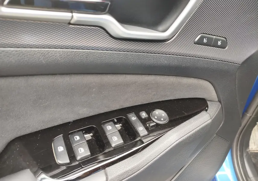 Gros plan sur la porte côté conducteur du Kia Sportage bleu, montrant les commandes des vitres et les réglages des sièges.