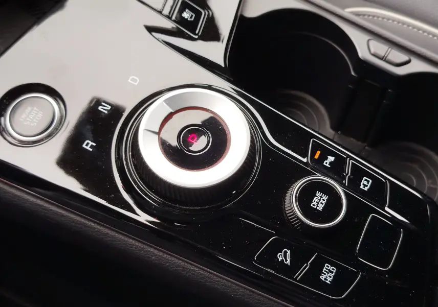 Gros plan sur la console centrale noire brillante du Kia Sportage 2022, avec sélecteur rotatif de boîte auto et boutons de contrôle.