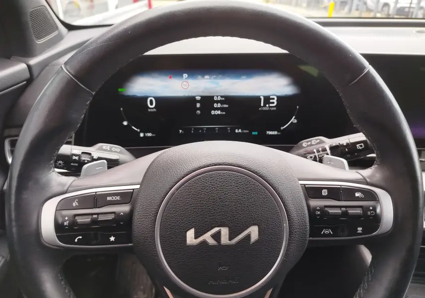 Vue rapprochée du volant noir du Kia Sportage 2022 avec tableau de bord numérique allumé en arrière-plan.