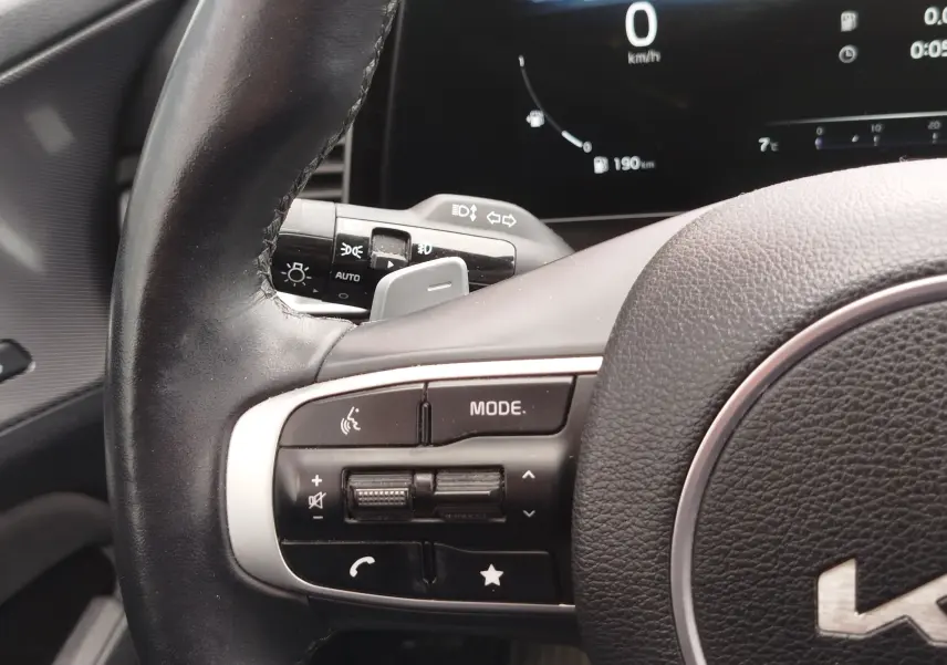 Gros plan sur le volant cuir noir côté gauche du Kia Sportage 2022 avec commandes multimédia et tableau de bord numérique.