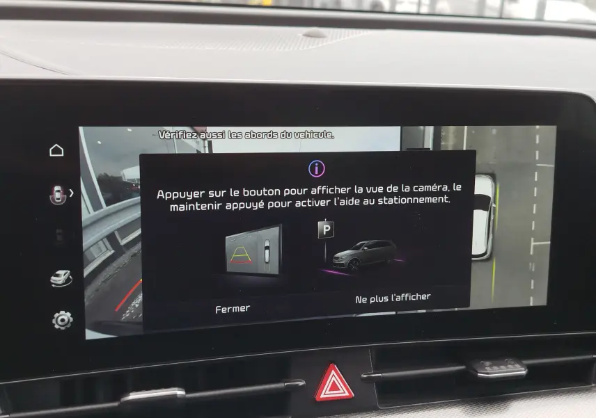 Écran tactile intérieur montrant l'aide au stationnement du Kia Sportage bleu, vue caméra 360° en affichage digital.