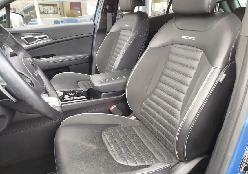 Vue intérieure côté conducteur du Kia Sportage bleu, sièges avant en cuir noir GT-Line avec surpiqûres blanches.