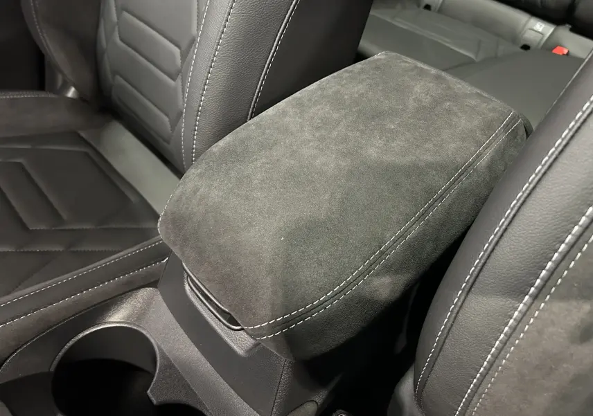 Gros plan sur l'accoudoir central en alcantara gris et cuir noir avec surpiqûres blanches dans l'habitacle du Nissan Qashqai.