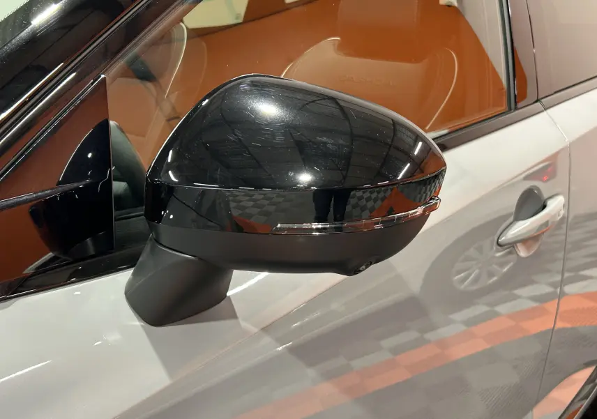 Rétroviseur noir brillant côté gauche du Nissan Qashqai gris céramique avec intérieur cuir marron visible.