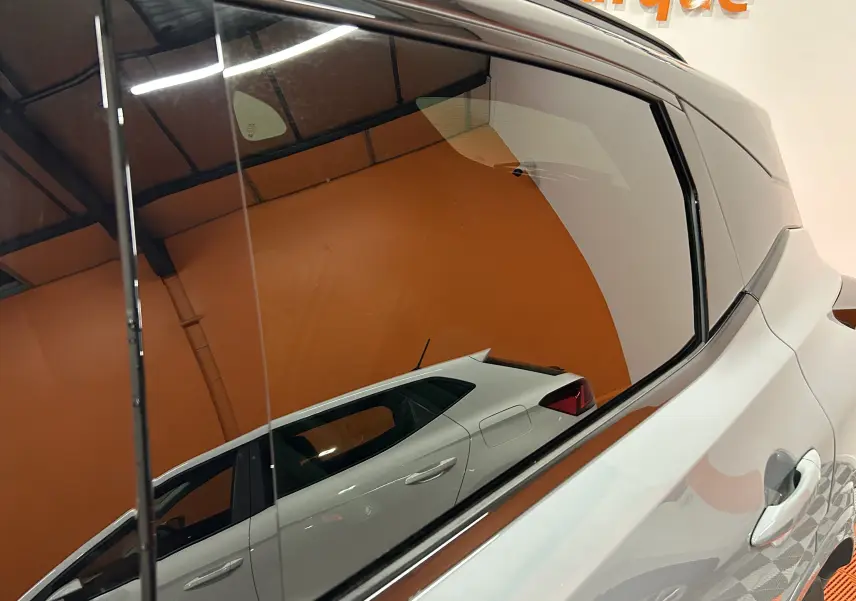 Reflet latéral droit du Nissan Qashqai 2025 gris céramique métal avec toit noir dans un intérieur orange.