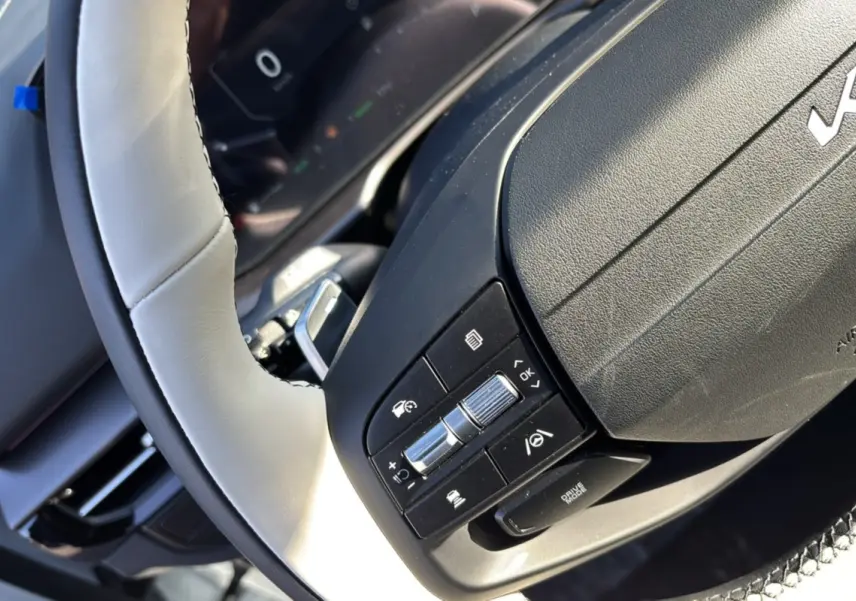 Gros plan sur le volant cuir beige clair du Kia Sportage 2026 avec commandes multifonctions et palettes au volant.