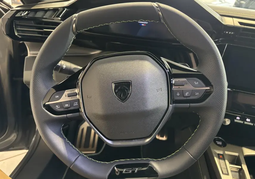 Volant GT en cuir noir avec surpiqûres vert Adamite dans l'habitacle du Peugeot 308 gris Selenium, vue de face rapprochée.