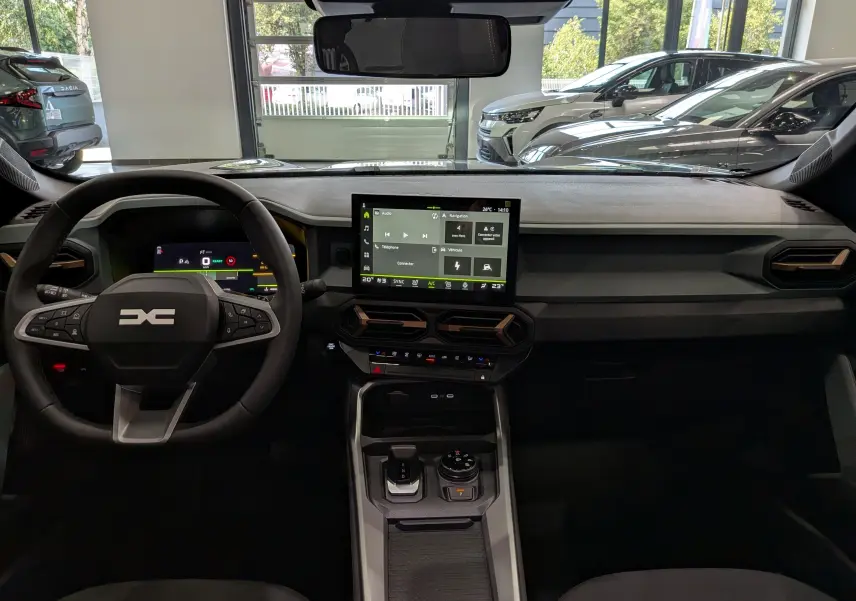Vue intérieure frontale du tableau de bord du Dacia Bigster Hybrid-G 150 avec écran tactile central et volant multifonction.