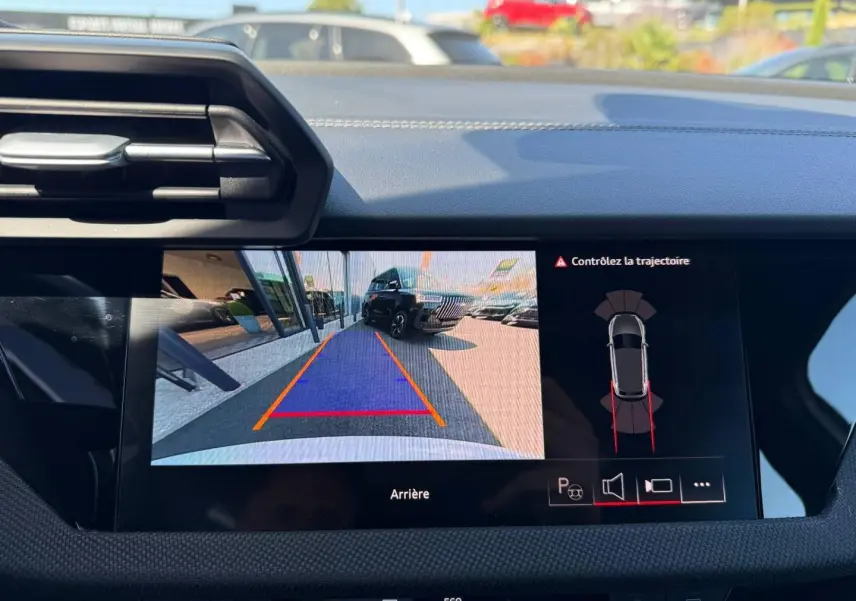 Écran central montrant la caméra de recul avec vue arrière d’un véhicule noir en stationnement, intérieur Audi A3 blanc.