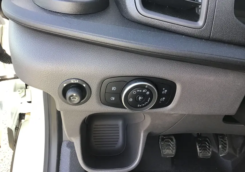 Gros plan sur les commandes d'éclairage et réglage du tableau de bord côté gauche dans un Ford Transit blanc avec boîte manuelle.