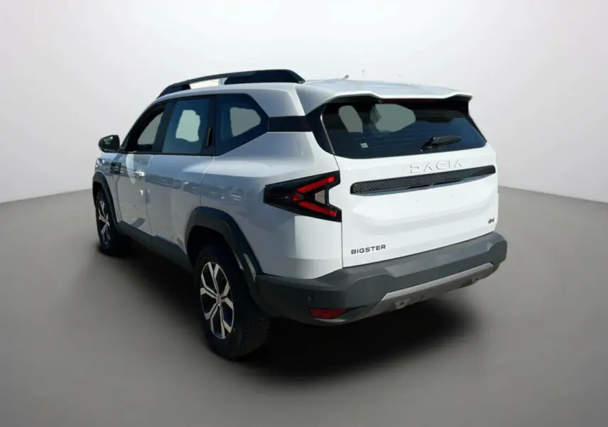 Vue 3/4 arrière droite du SUV Dacia Bigster blanc glacier avec feux arrière en forme de flèche et barres de toit noires.