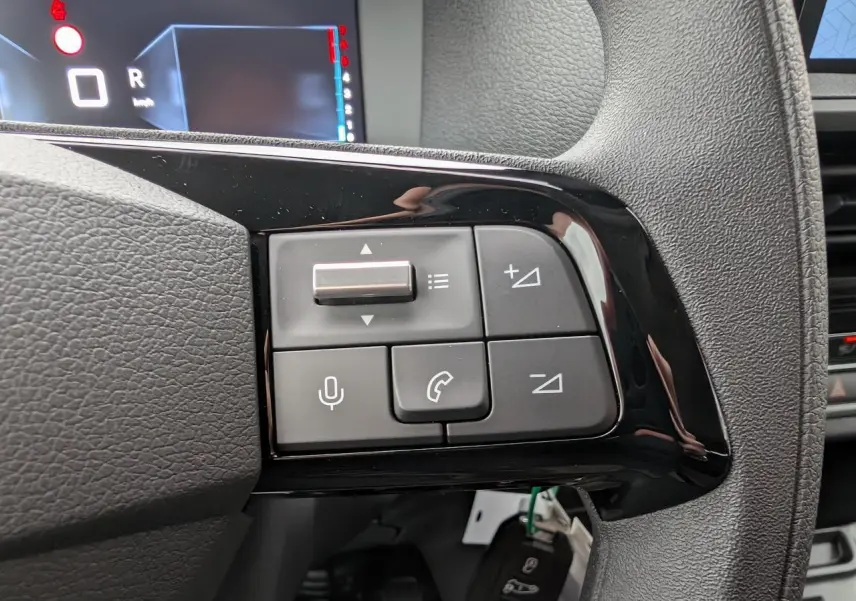 Gros plan sur les commandes au volant noir brillant du Citroën Jumpy gris, avec affichage numérique en arrière-plan.