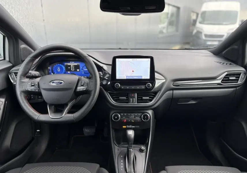Vue intérieure avant du Ford Puma 2023, tableau de bord noir avec écran tactile GPS et volant ST-Line perforé.