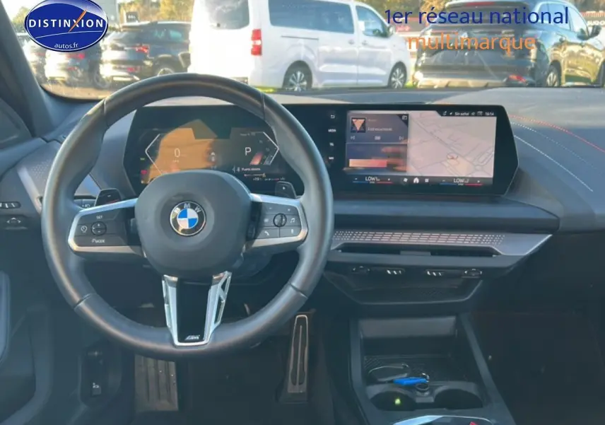 Vue intérieure avant de la BMW Série 1 blanche, volant M sport et écran tactile central avec navigation affichée.