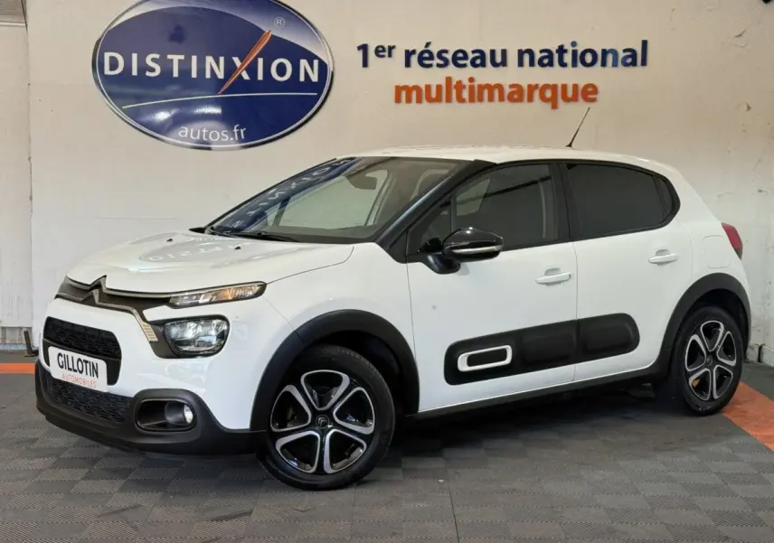 Citroën C3 blanche vue 3/4 avant droit, avec protections latérales noires et jantes stylisées bicolores.