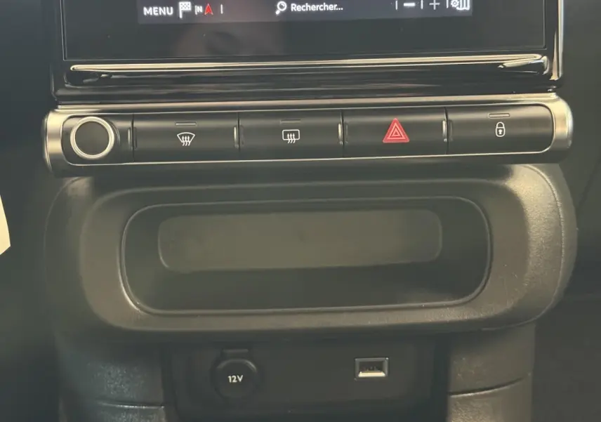 Vue rapprochée de la console centrale noire de la Citroën C3 blanche, avec commandes et prise 12V visible.