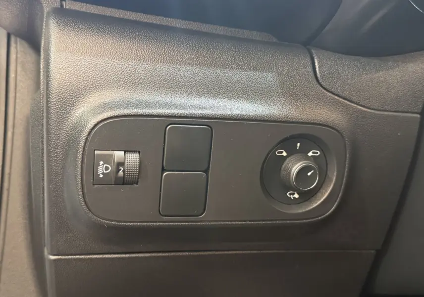 Gros plan sur les commandes noires de réglage des phares et des rétroviseurs dans une Citroën C3 blanche, côté conducteur.