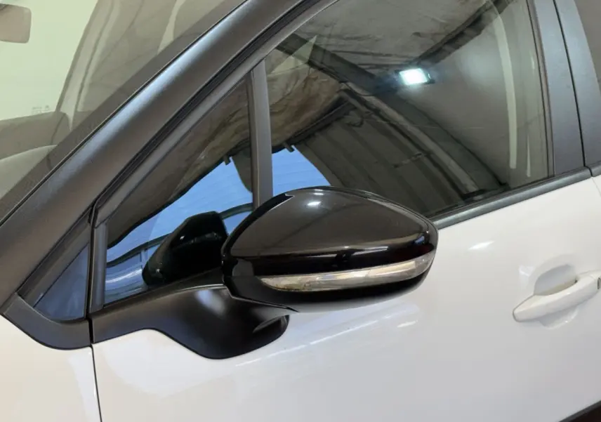 Gros plan sur le rétroviseur noir brillant côté conducteur d'une Citroën C3 blanche, avec la porte avant visible.