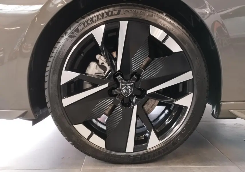 Gros plan sur la jante alliage 18" bi-ton noir et argent avec logo Peugeot, sur roue avant droite gris sélénium.