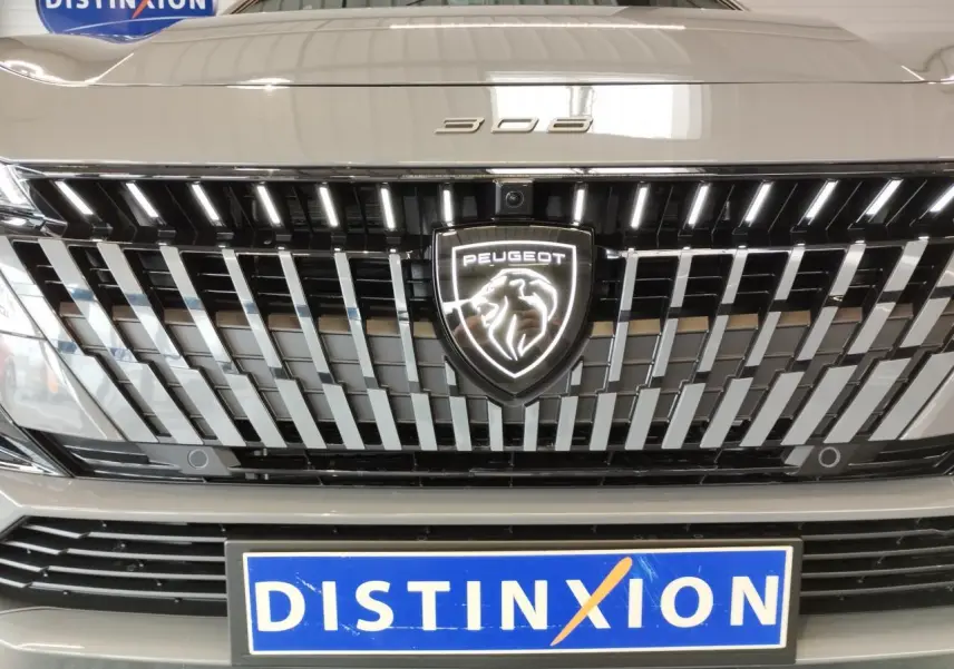 Gros plan sur la calandre avant gris selenium du Peugeot 308 avec logo lion lumineux et plaque Distinxion.