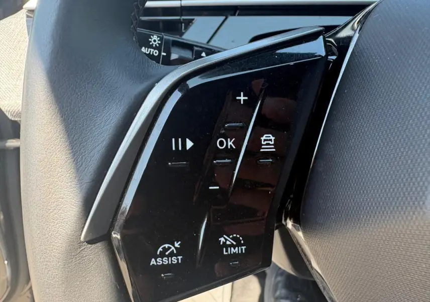 Gros plan sur les commandes noires au volant du Peugeot 3008 gris, version Hybrid 145 e-DCS6 Allure 2025.