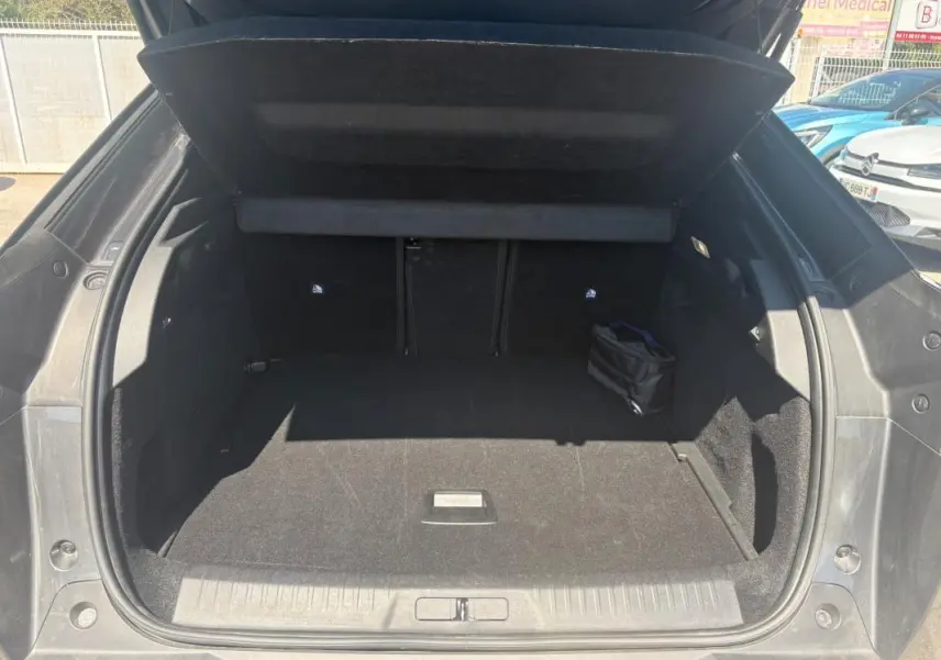 Coffre ouvert vu de l'arrière d'un Peugeot 3008 Hybrid gris, espace de chargement vide avec petit sac noir à droite.
