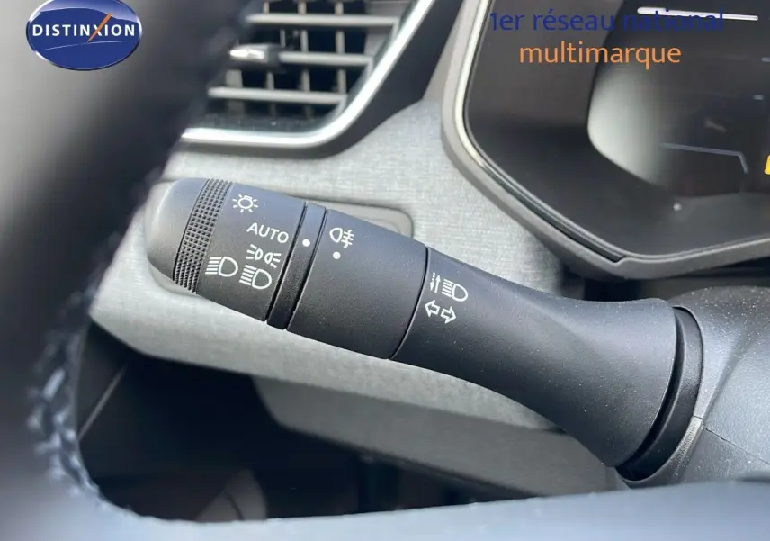 Gros plan sur la commande des feux et clignotants à gauche du volant dans l'habitacle d'une Renault Clio noire.