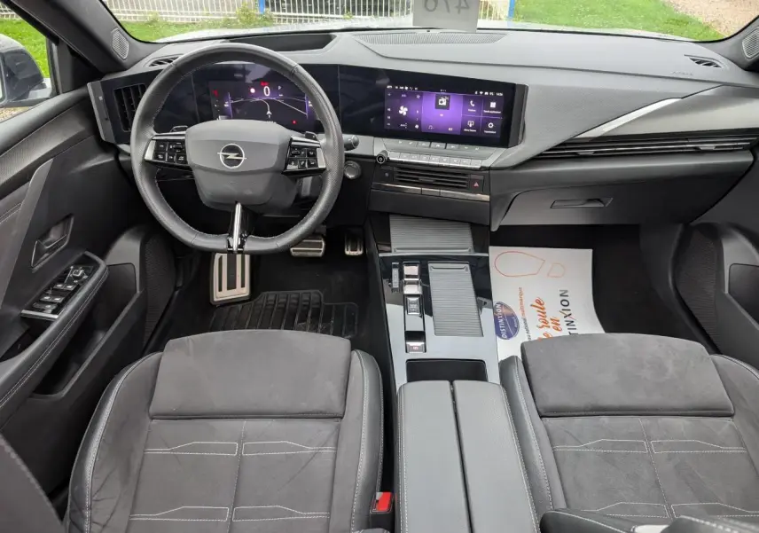Intérieur avant d'une Opel Astra 2024, sellerie mixte noire, volant cuir, tableau de bord digital et écran tactile central.