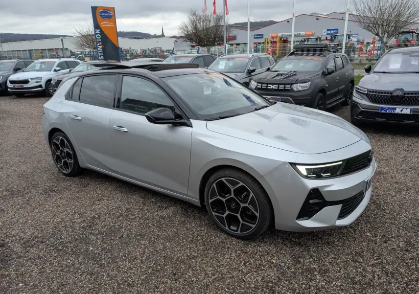 Opel Astra 2024 gris métallisé vue 3/4 avant avec toit noir panoramique et jantes alliage 18 pouces pentagonales.