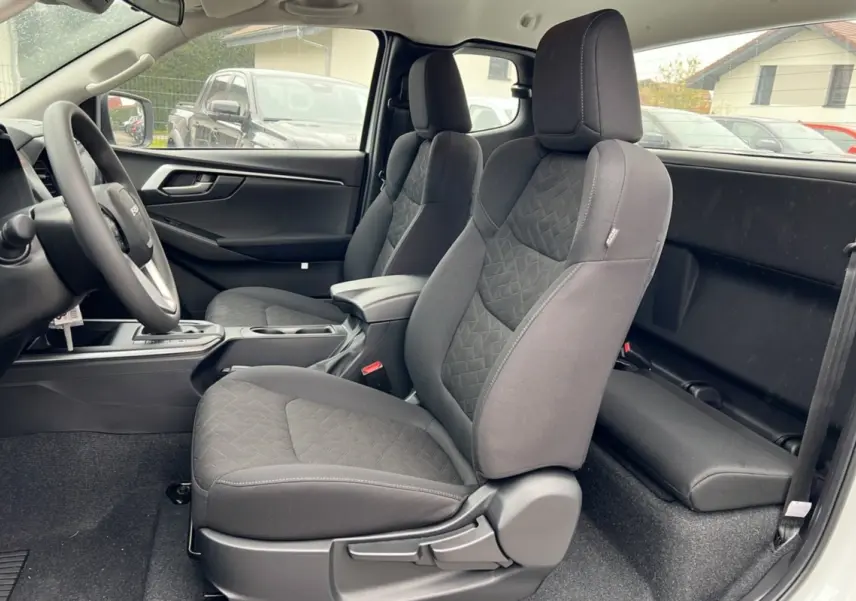 Vue intérieure côté gauche du pick-up Isuzu D-MAX 2026 Splash White, montrant les sièges avant en tissu gris et l'accoudoir central.