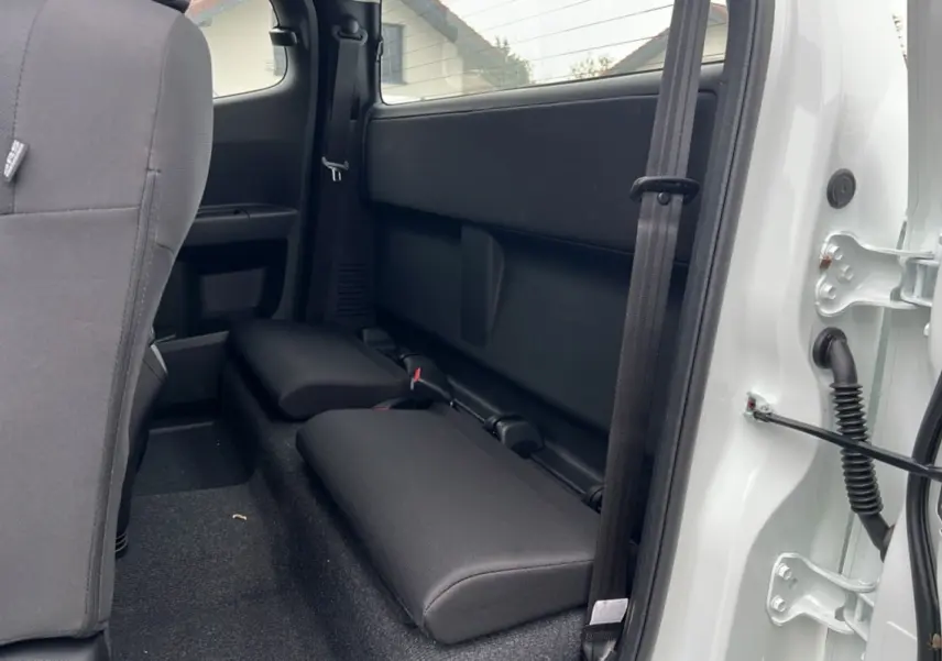 Vue intérieure arrière côté droit du pick-up Isuzu D-MAX Splash White 2026 avec sièges strapontins noirs et portière ouverte.