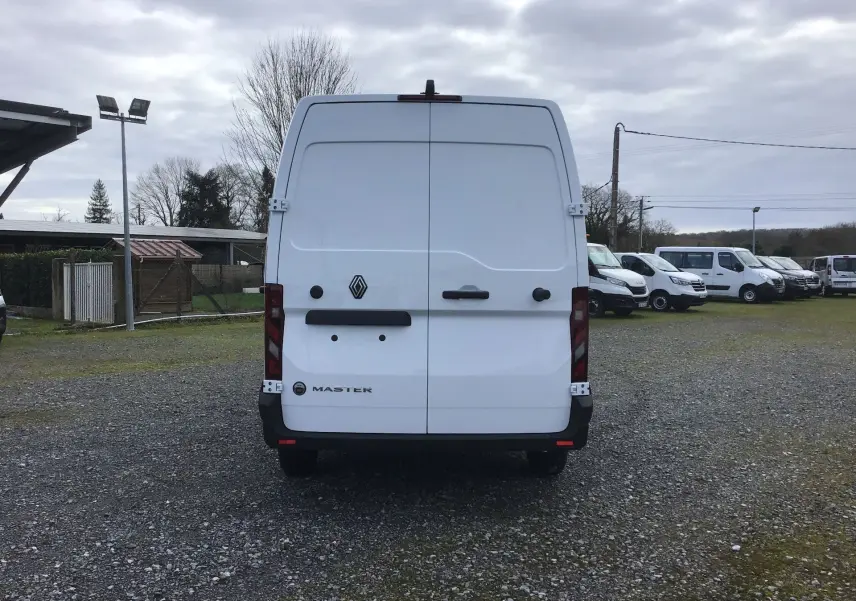 Vue arrière d’un utilitaire Renault Master blanc, portes battantes fermées, sur un parking extérieur avec plusieurs autres véhicules.