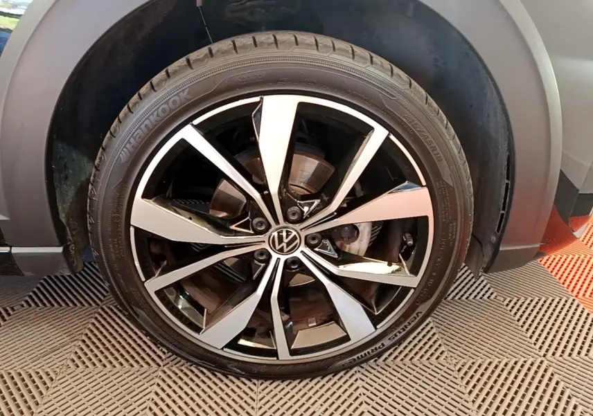 Gros plan sur la roue avant droite du Volkswagen Taigo noir 2023, mettant en valeur la jante alliage bicolore et le logo VW central.