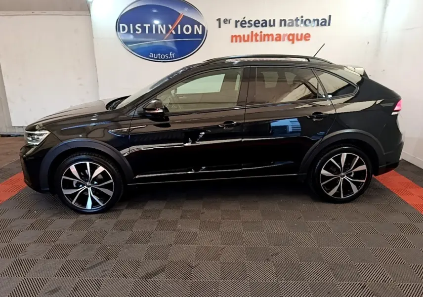 Profil côté gauche du Volkswagen Taigo noir 2023 R-Line avec jantes alliage et rails de toit noirs dans un showroom.