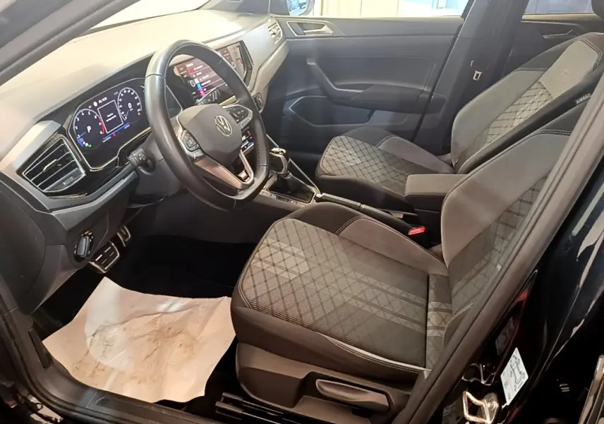 Vue intérieure côté conducteur du Volkswagen Taigo noir 2023, sièges tissu à motifs et tableau de bord digital.