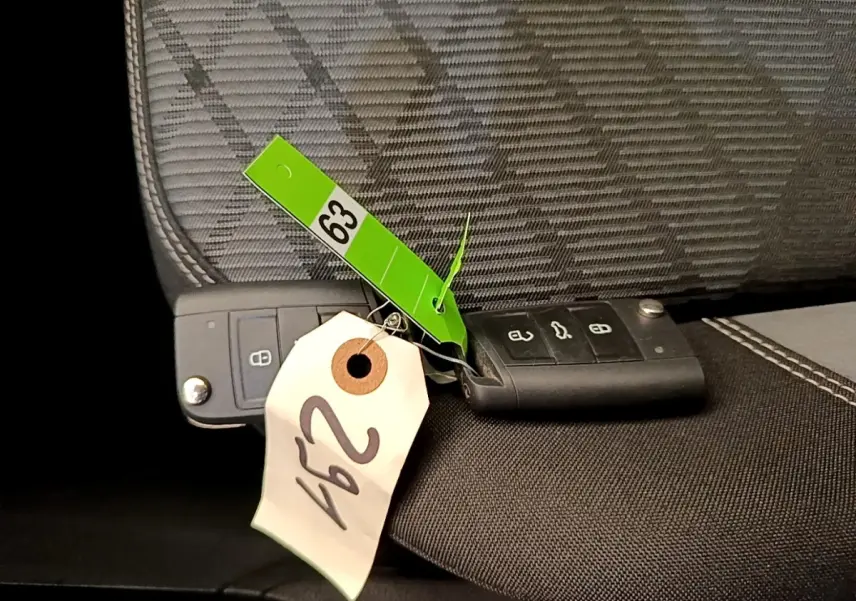 Gros plan sur deux clés noires Volkswagen posées sur un siège tissu gris et noir avec étiquettes numérotées.