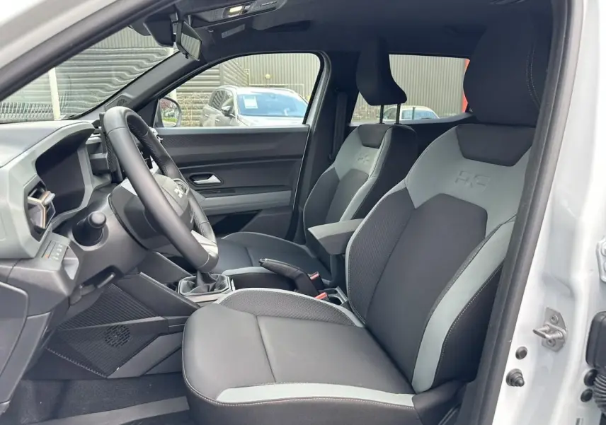 Vue intérieure côté conducteur du Dacia Duster blanc glacier 2025, montrant les sièges avant bi-ton et le volant.