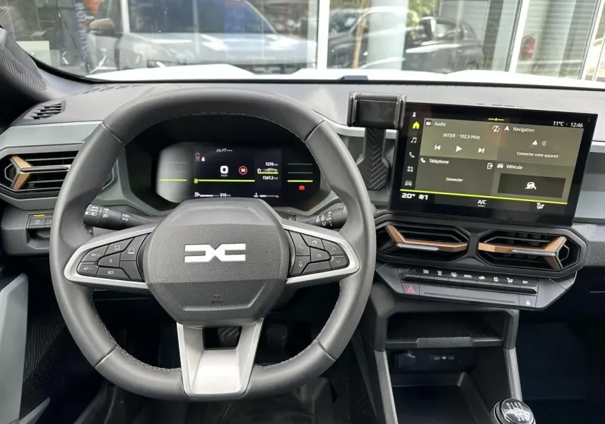 Vue intérieure centrée sur le volant et le tableau de bord numérique du Dacia Duster blanc glacier 2025.