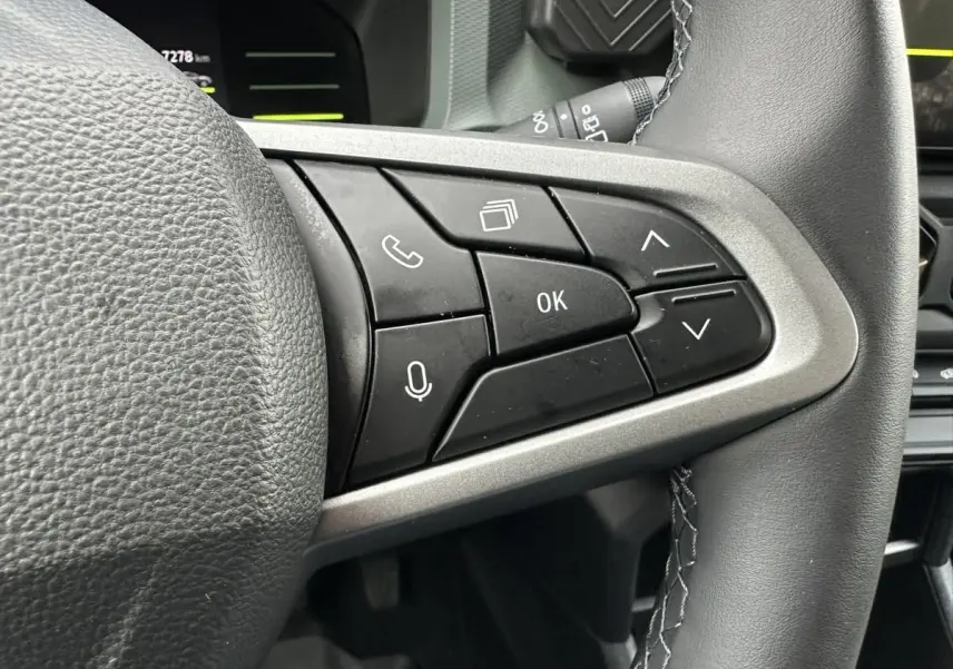 Gros plan sur les commandes au volant à droite du DACIA Duster blanc glacier, montrant les boutons multifonctions et la finition cuir.