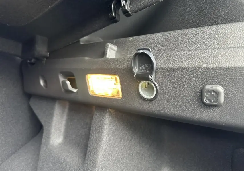 Détail de la prise 12V et de l'éclairage intérieur dans le coffre du Dacia Duster blanc glacier 2025.