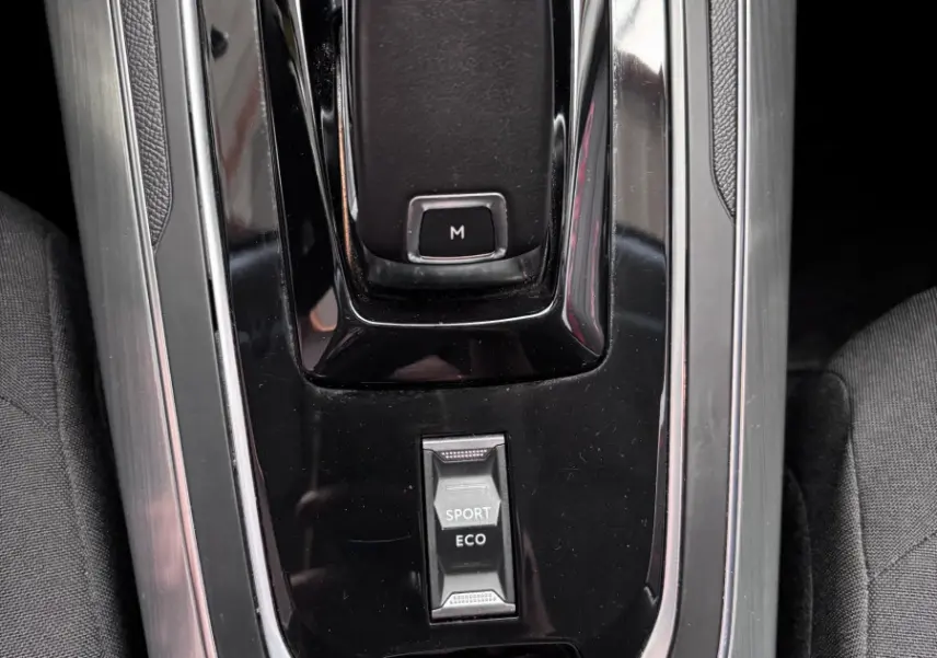 Vue rapprochée de la console centrale noire et grise avec levier de vitesses automatique et bouton modes Sport/Eco d'une Peugeot 308 gris foncé.