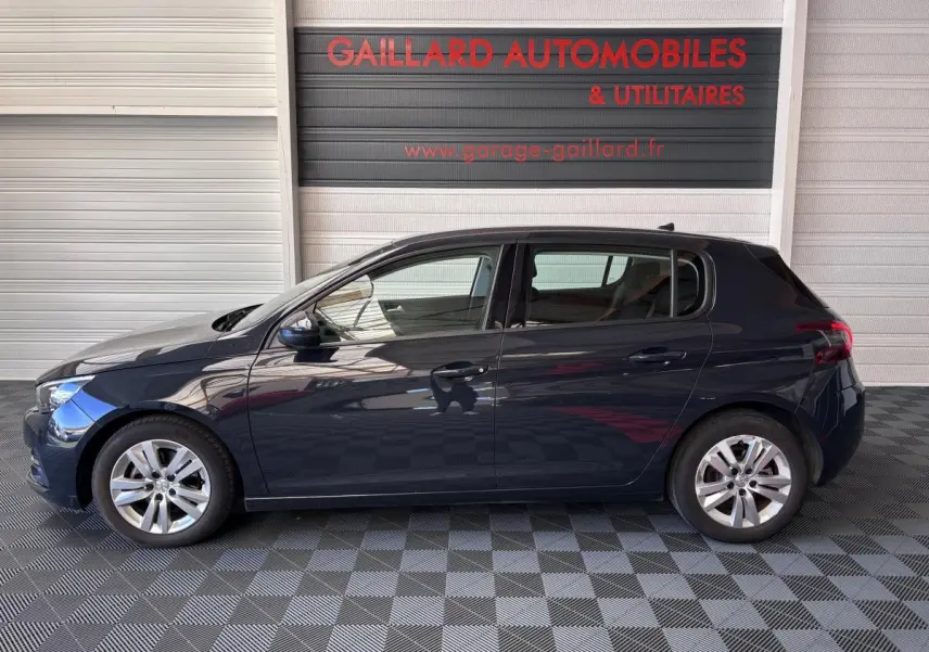 Profil côté gauche d'une Peugeot 308 gris foncé 2019 garée devant un mur avec logo Gaillard Automobiles.