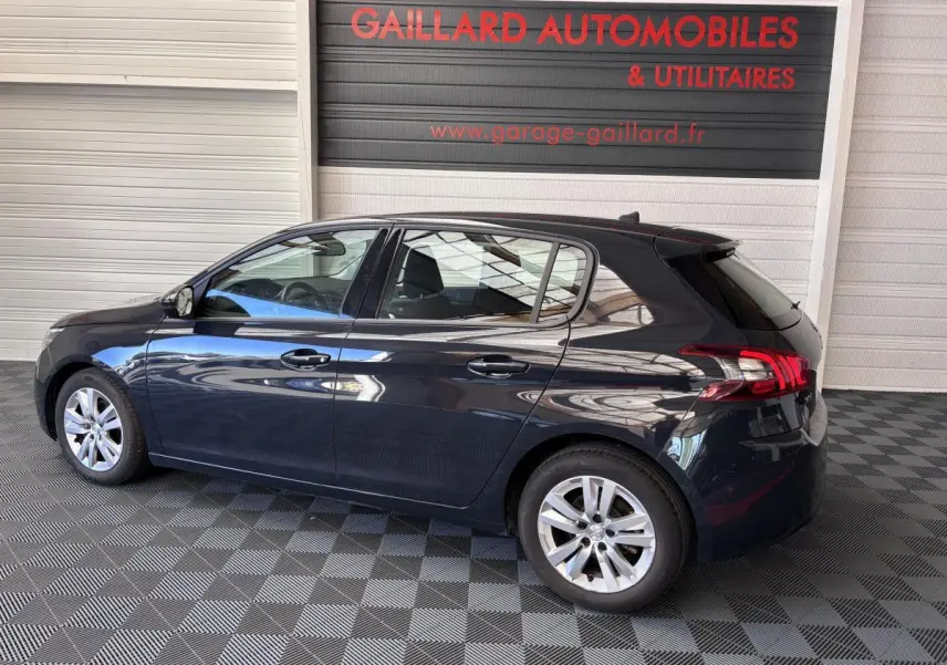 Peugeot 308 gris foncé vue de profil côté gauche dans un garage avec sol à damier noir et gris.