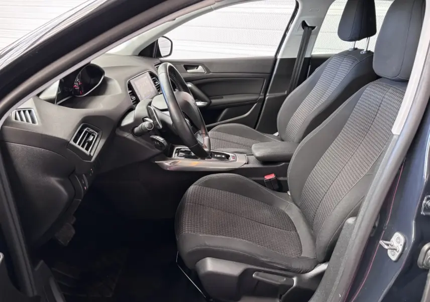 Intérieur avant droit d'une Peugeot 308 gris foncé, montrant sièges tissu, volant et console centrale moderne.