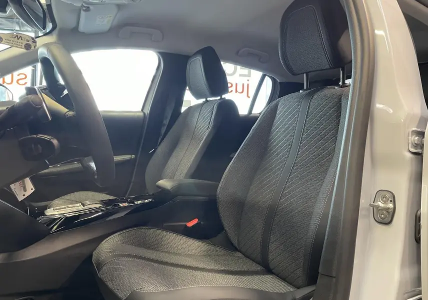 Vue intérieure côté conducteur de la PEUGEOT 208 blanche, mettant en valeur les sièges tissu gris et l'accoudoir central.